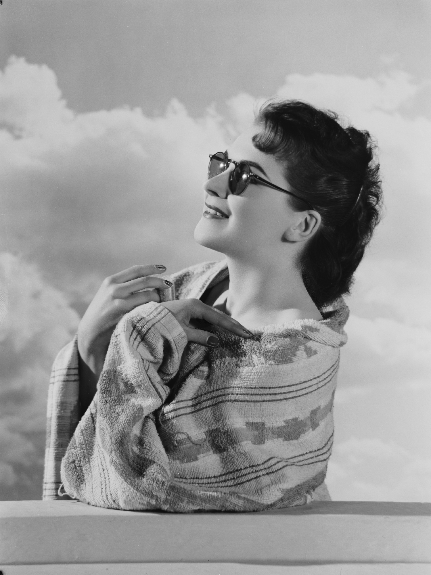 A photograph of a young woman wrapped in a towel wearing a pair of sunglasses