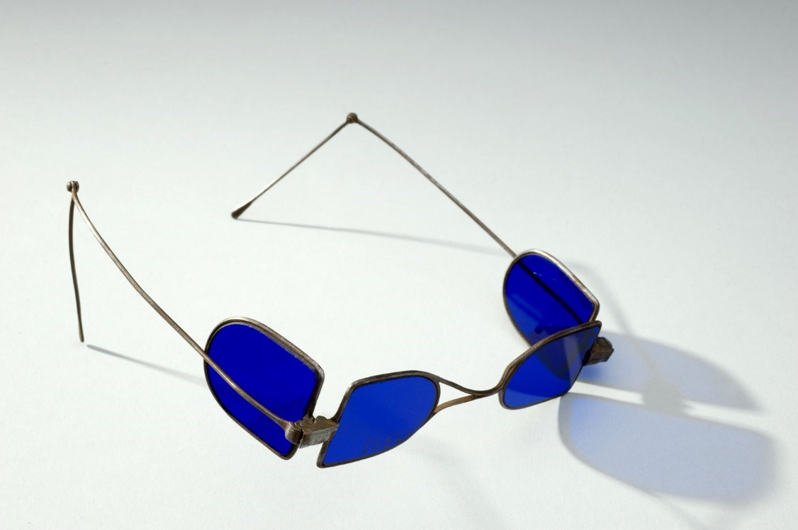 Turn pin spectacles, steel wire, eye preservers, double folding lenses, tinted, French(?), 1790-1850. Full view, side angle, pale grey background