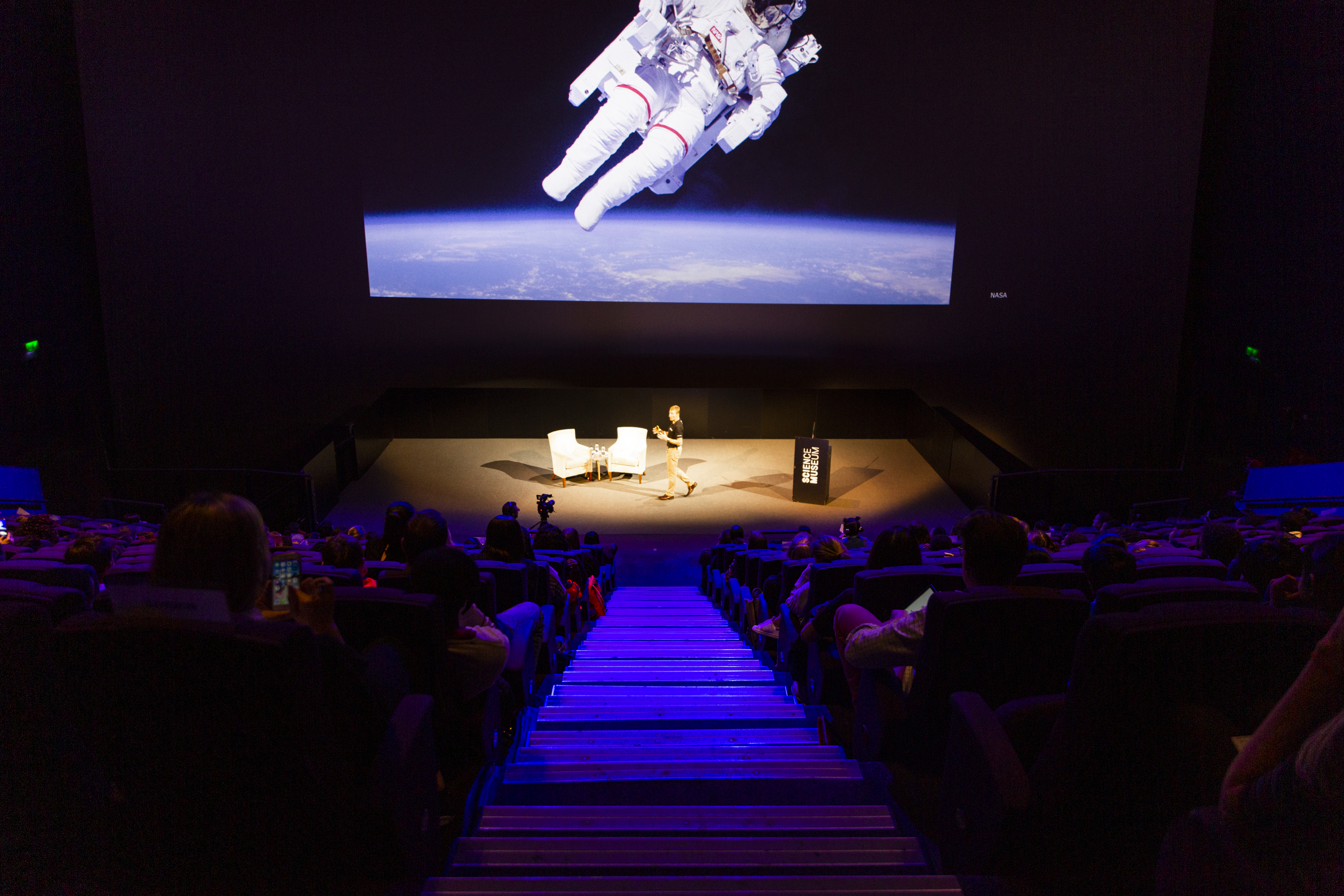 Tim Peake speaking on stage in the Science Museum's IMAX auditorium.