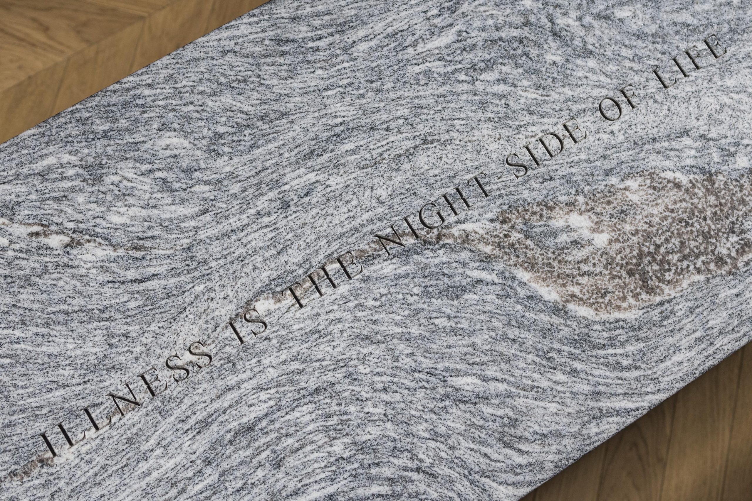 Grey stone bench with "illness is the night side of life" engraved on the top