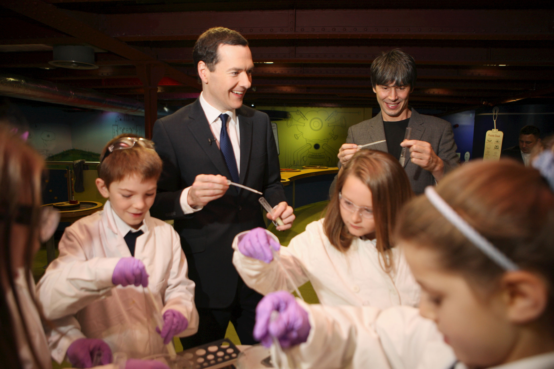 Professor Brian Cox and the Chancellor conduct a bioluminescence experiment with local school children. 
