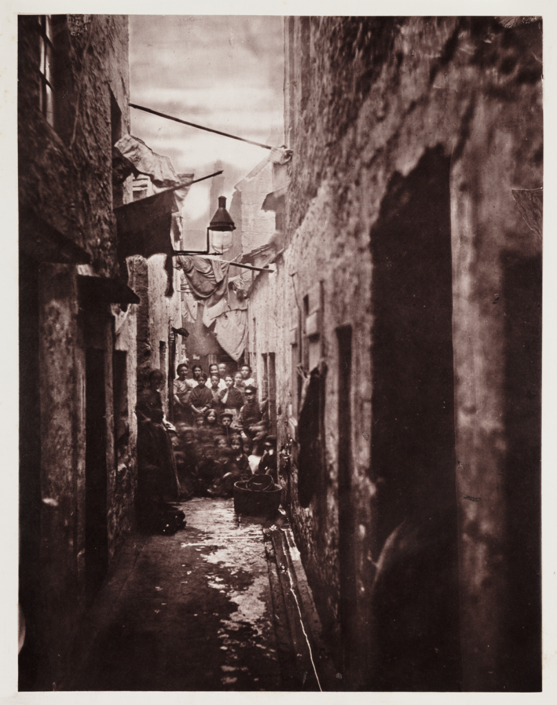 Crowd of women and children gathered together behind No. 118 High Street in Glasgow, taken by Thomas Annan in 1868. 