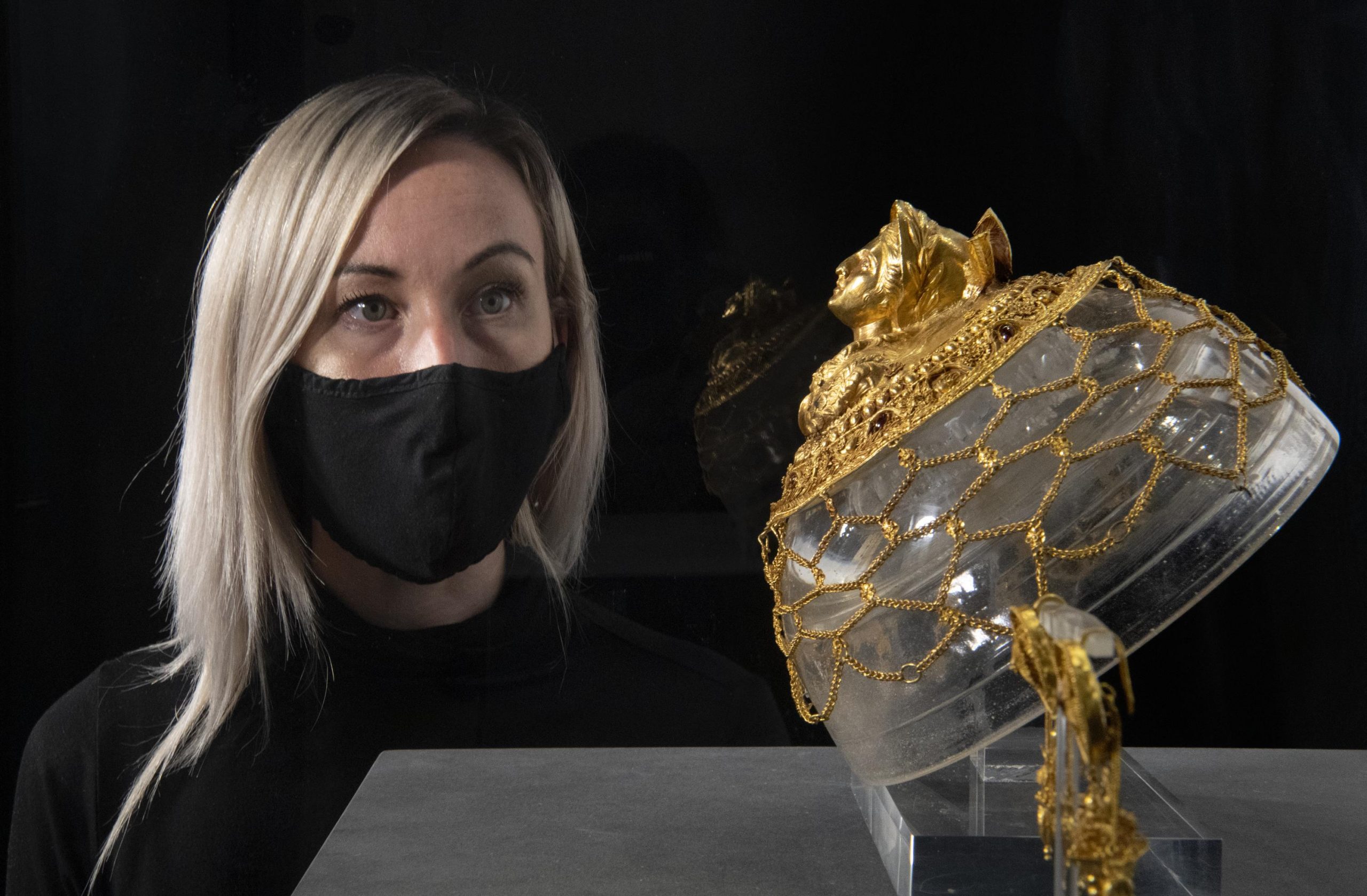 A visitor peers at the gold headdress and earrings decorated with imagery of Athena and the Muses 