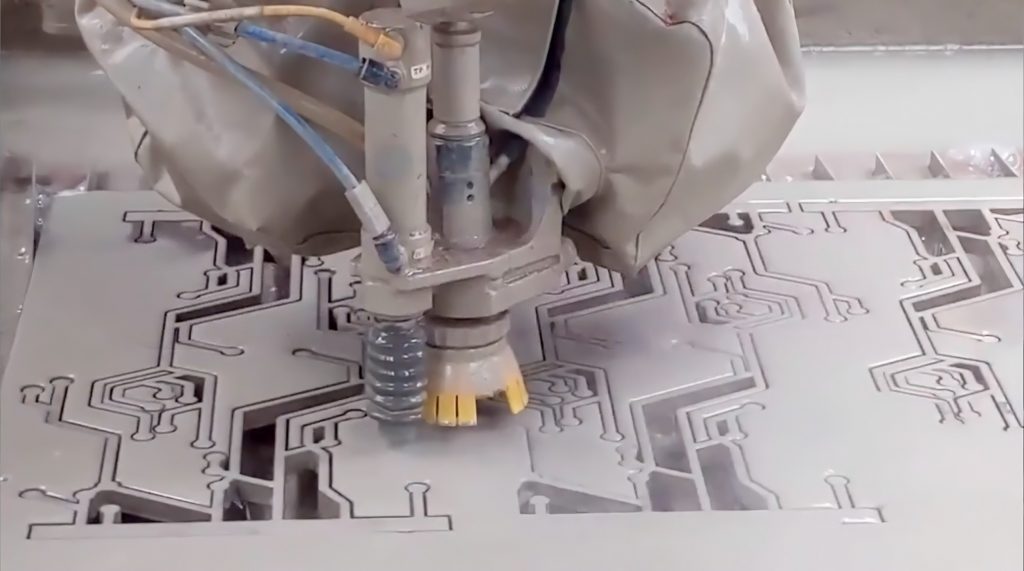 A light grey waterjet cutting a design pattern into an aluminum sheet